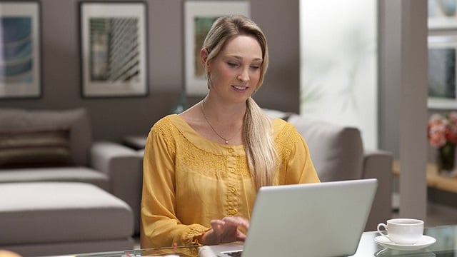 Woman using laptop with cup of coffee nearby.